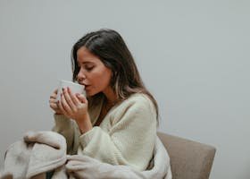 Woman wrapped in a blanket, sipping from a mug, enjoying a relaxing moment indoors.